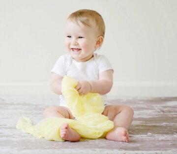 Χαμογελαστό μωρό κάθεται με άνετα βρεφικά ρούχα σωστού μεγέθους σε λευκό φόντο